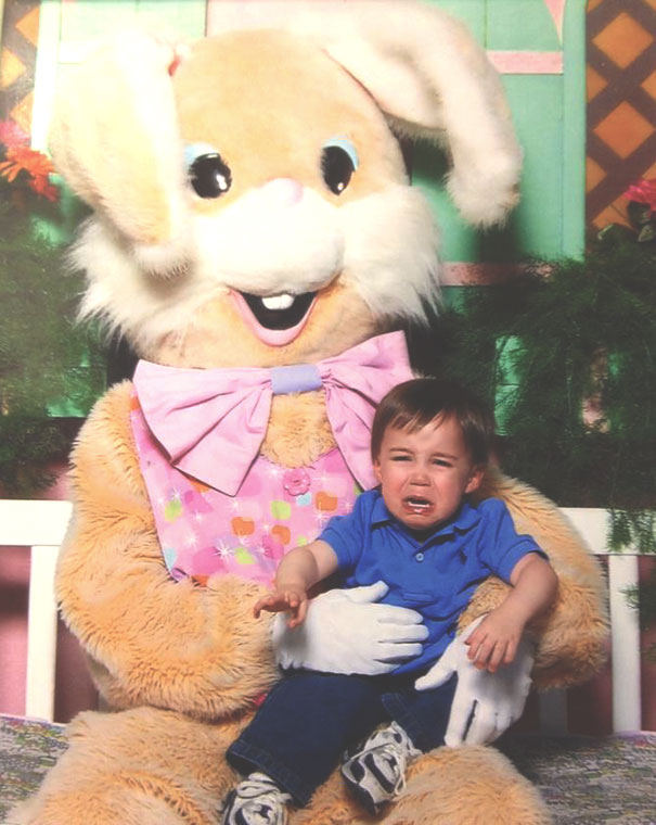 Crying child on the lap of a vintage Easter Bunny with large bowtie in a colorful setting.