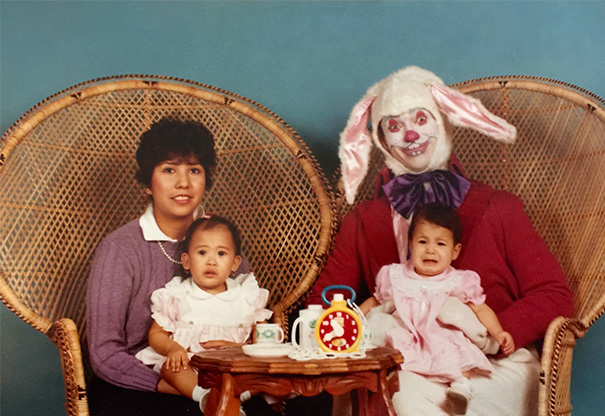 Family with vintage Easter Bunny, two children on laps, wicker chairs, vibrant setting.