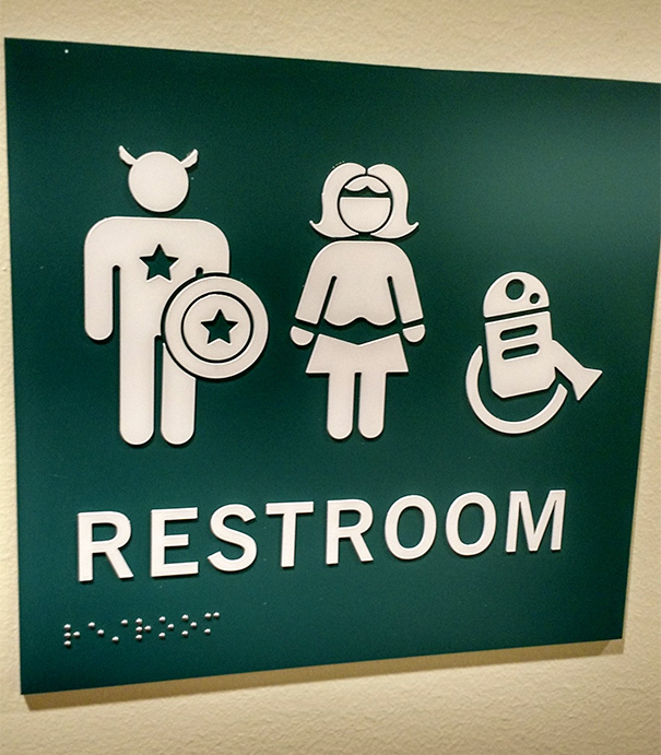 Funny bathroom sign with superhero-themed restroom symbols.