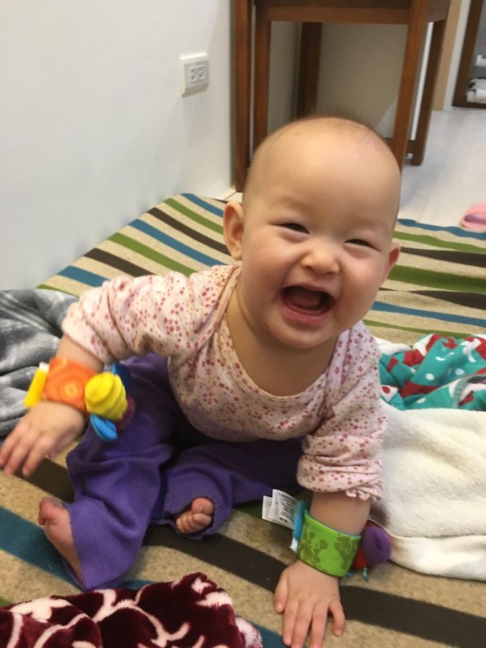 Happy baby crawling on striped rug wearing colorful wrist rattles, illustrating kids as copy-paste versions of their parents.