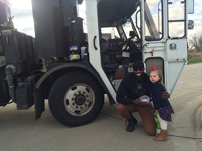 Man posing with a girl in front of a garbage truck 