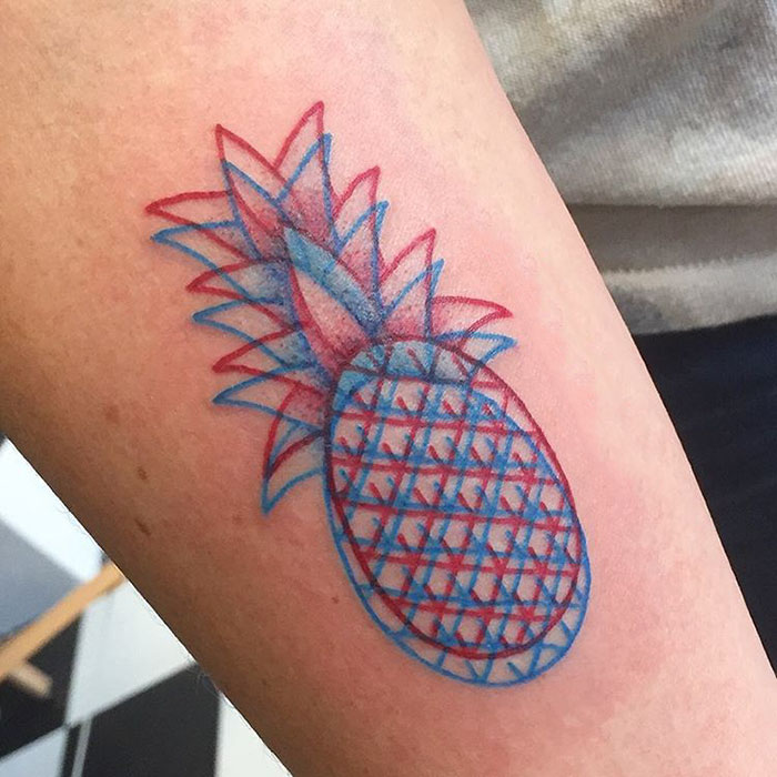 3D-inspired tattoo of a pineapple on a forearm, featuring overlapping red and blue geometric patterns.