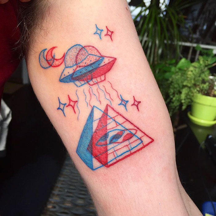 3D-inspired tattoo of a UFO and pyramid in red and blue ink on a person's arm, showcasing trendy ink art.