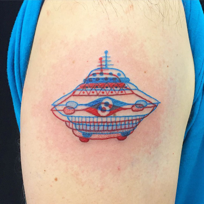 3D-inspired tattoo of a UFO design in blue and red ink on a person's arm.