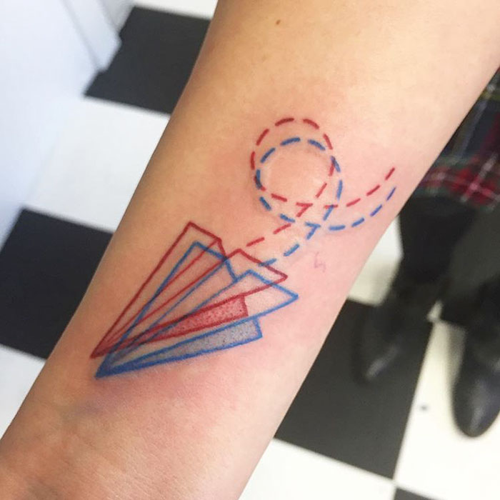 3D-inspired tattoo of a paper airplane with red and blue dashed lines on an arm, showcasing the latest ink trend.