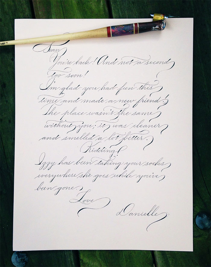 Beautiful handwriting on a letter with a calligraphy pen resting on top.