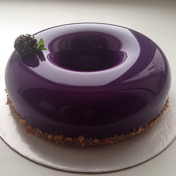 Glossy purple cake with a perfect mirror glaze, topped with a blackberry, satisfying every perfectionist's soul.