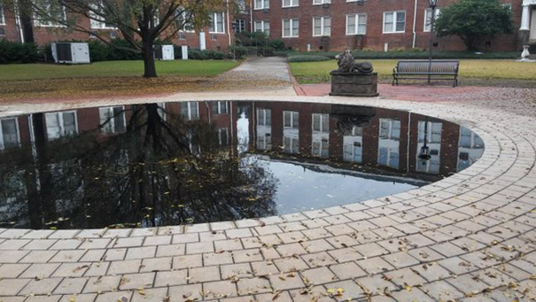 Perfectly reflective pond surrounded by circular paving stones in a courtyard, capturing a flawless mirror image of the building.