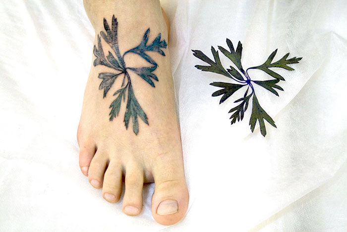 Botanical tattoo on a foot using a real leaf as a stencil, showcasing intricate plant design.