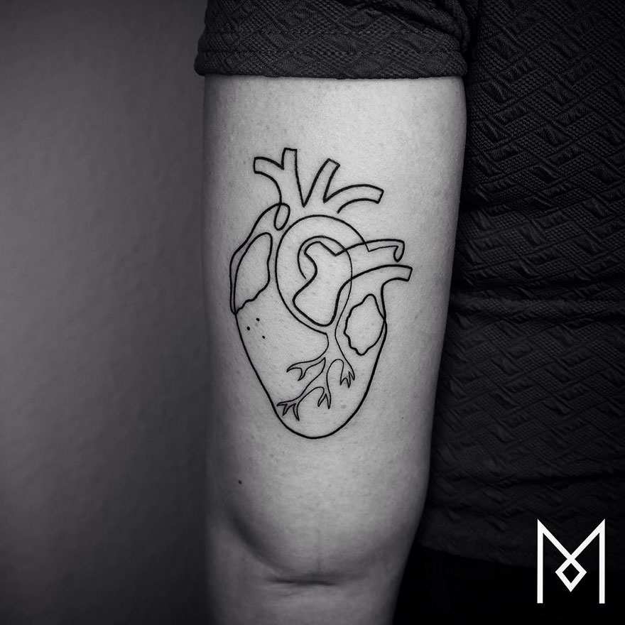 Minimalist single line tattoo of an anatomical heart on a person's arm.