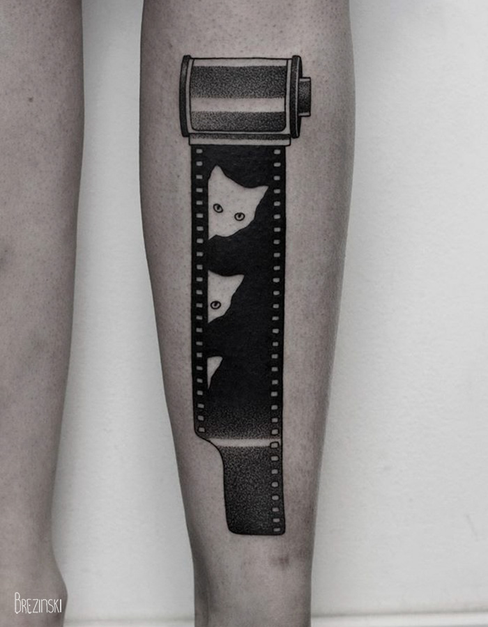 Surreal tattoo of a film roll with cat faces by Belarussian artist Ilya Brezinski on forearm.