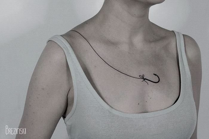 Surreal tattoo by Belarussian artist on a person's collarbone, featuring a minimalist hook design.