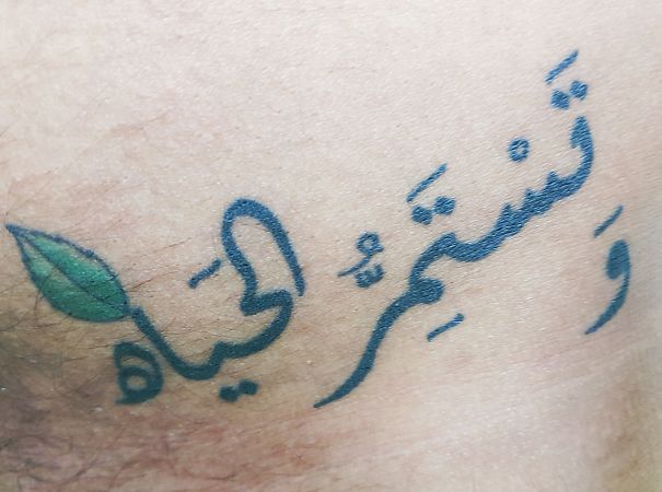 Arabic script tattoo with a green leaf symbolizing hidden meaning.