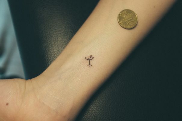 Minimalist small foot tattoo of a cocktail glass next to a coin on skin.