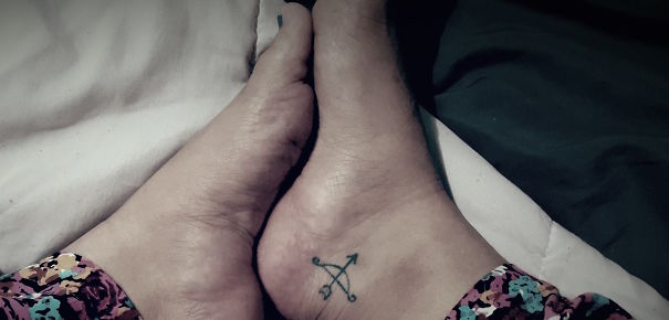 Small foot tattoo with an arrow design, showcasing minimalist ink art on the ankle.