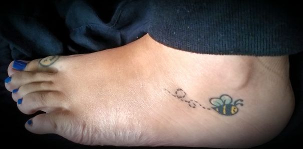 Small foot tattoo of a bee with a dotted flight path, showcasing a minimalist design.