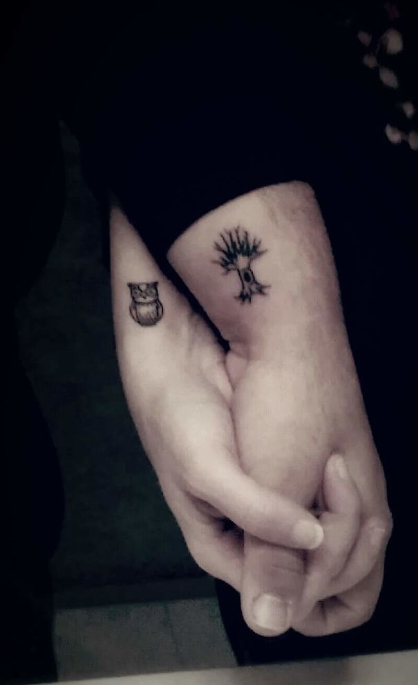 Two wrists with clever tattoos of an owl and a tree, symbolizing hidden meanings.