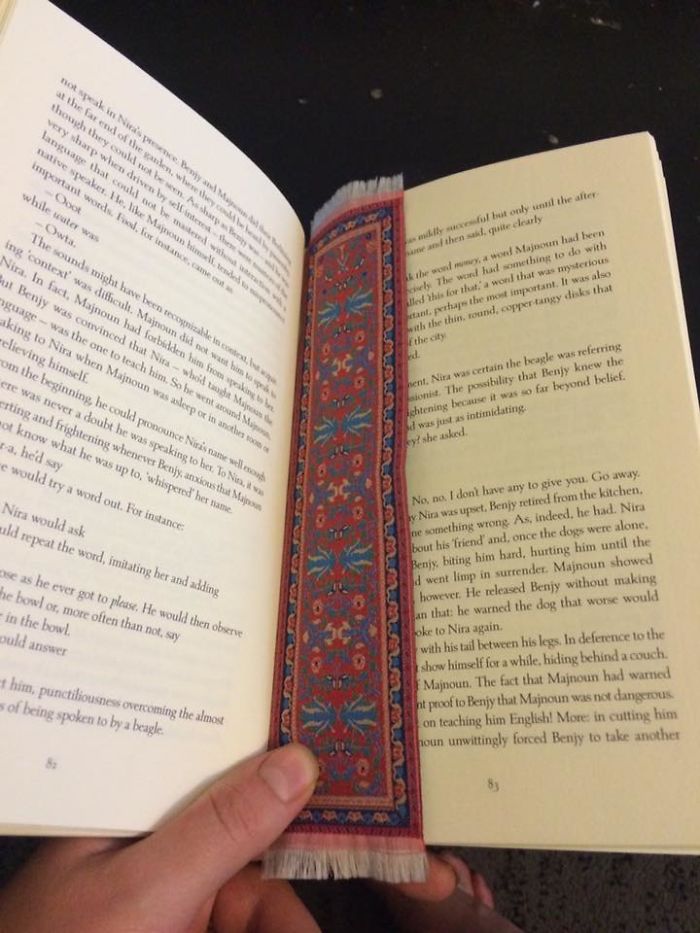 Person holding a book open with a tiny carpet bookmark, showcasing a regrettable online purchase.