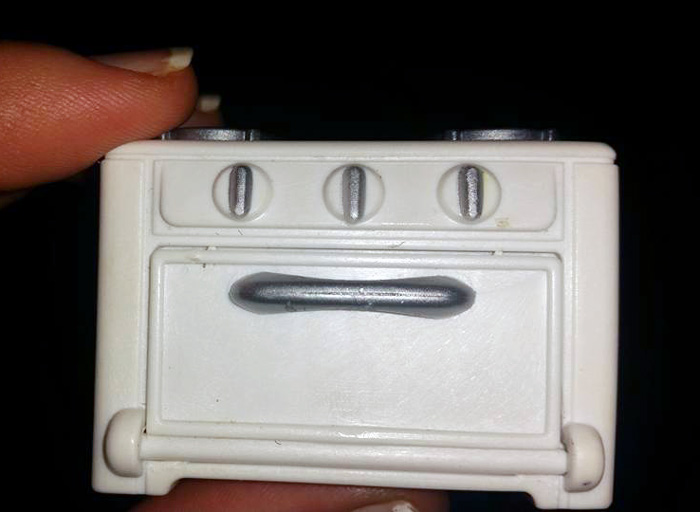 A regretted online purchase of a small, toy oven being held between fingers.