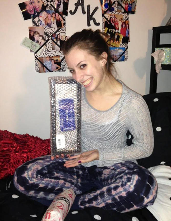 Person smiling while holding an online purchase in a bedroom, indicating possible regret over the product.