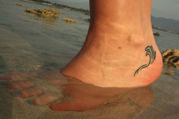 Small foot tattoo of a wave, partially submerged in water, showcasing minimalist design.