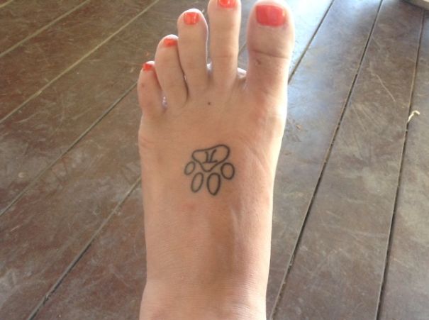 Small foot tattoo idea featuring a simple paw design on a foot with orange-painted toenails.
