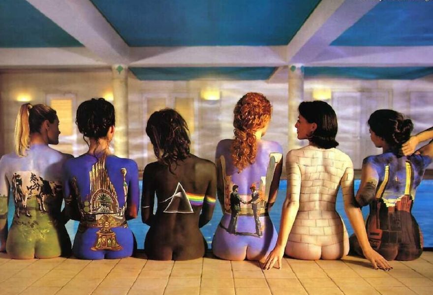 Six women with body art resembling classic album covers sit by a pool.
