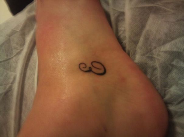 Minimalist small foot tattoo featuring an elegant swirl design.