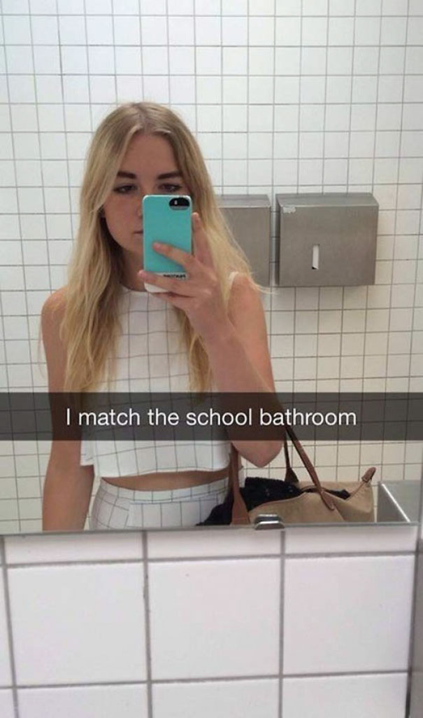 Woman in a tiled bathroom taking a selfie, wearing a matching outfit. Hilarious Snapchat moment.