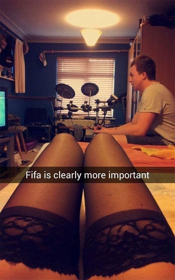 Man absorbed in playing FIFA while woman in lace stockings watches, capturing funny Snapchat moments.