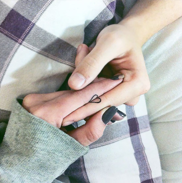 Two hands holding each other with a small, clever heart tattoo on a finger, symbolizing hidden meaning.