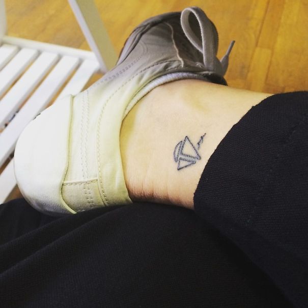 Minimalist small foot tattoo of a paper airplane on the ankle, emphasizing that less is more in tattoo design.