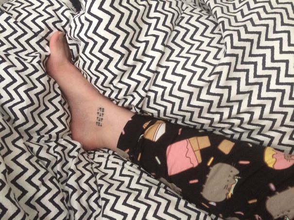 Small foot tattoo on ankle surrounded by patterned sheets, showcasing minimalist ink design.