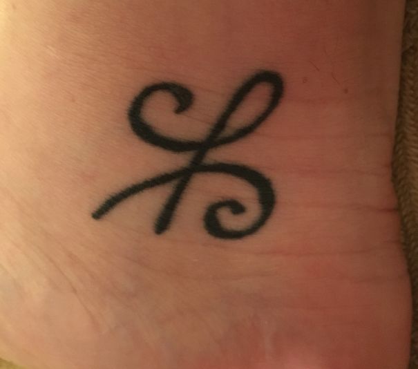 Minimalistic small foot tattoo with a simple black swirl design.