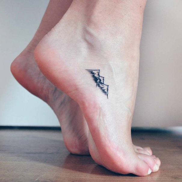 Minimalist small foot tattoo on ankle, featuring mountain design.