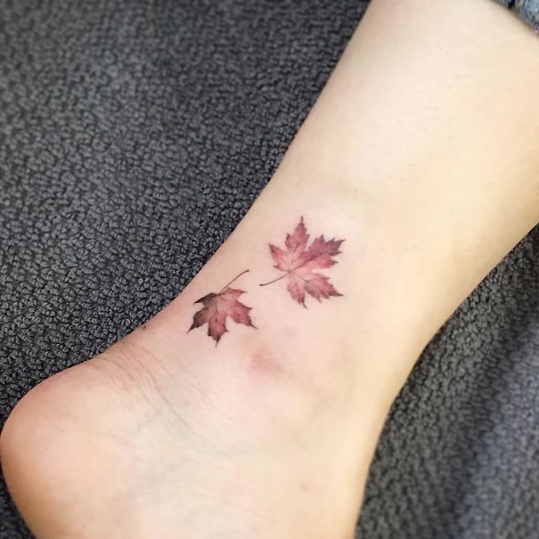 Small foot tattoo of two autumn leaves, showcasing minimalist design on the ankle.