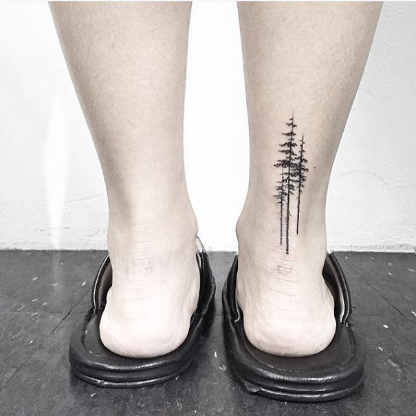 Minimalist small foot tattoo of tall trees on the back of ankles, showcasing how less is more in design.