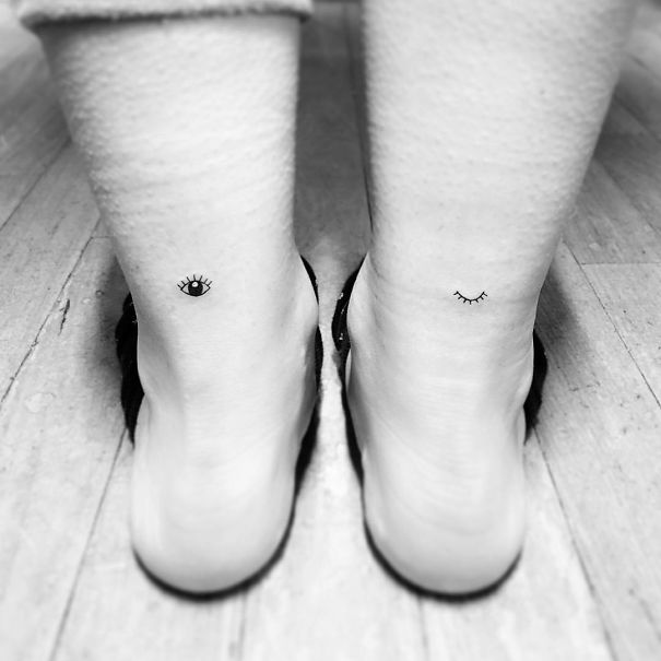 Minimalist small foot tattoos of eyes on both heels, showcasing "less is more" design.