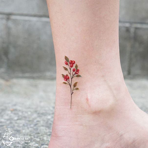 Small foot tattoo of a delicate branch with red berries, minimalist design showcasing that less is more.