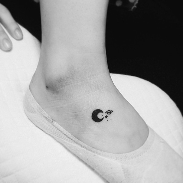 Minimalist small foot tattoo featuring a moon, planet, and stars.