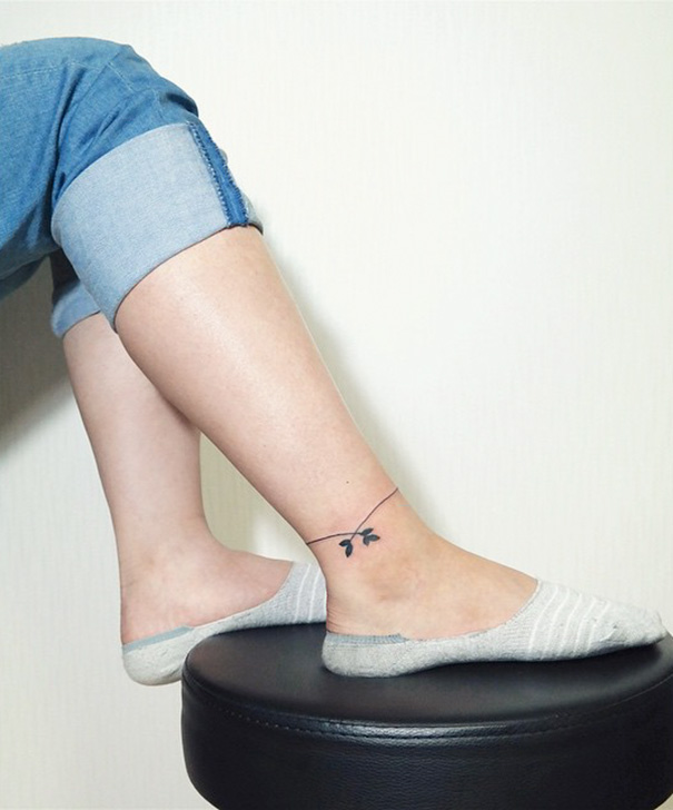 Minimalist small foot tattoo featuring a delicate branch, embodying the less is more aesthetic.