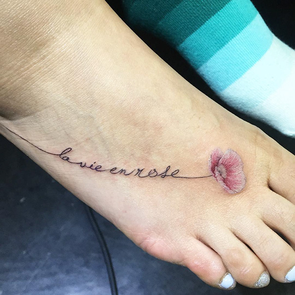 Small foot tattoo with "la vie en rose" text and a pink flower, showcasing minimalist tattoo ideas.