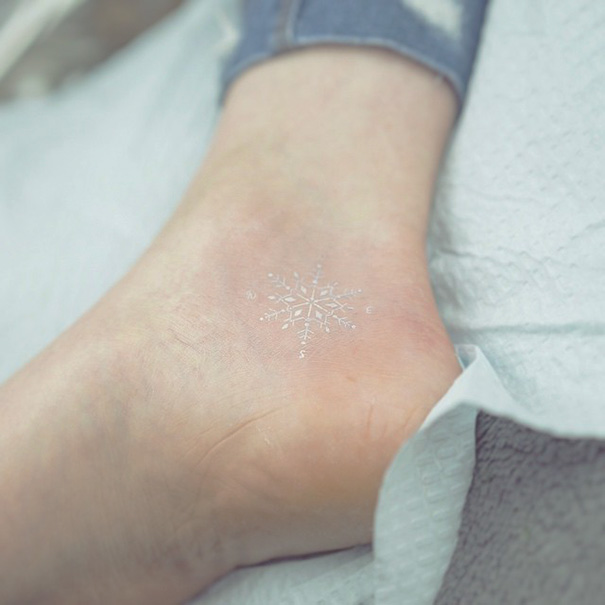 Minimalist small foot tattoo with a delicate white ink snowflake design, highlighting the concept of less is more.