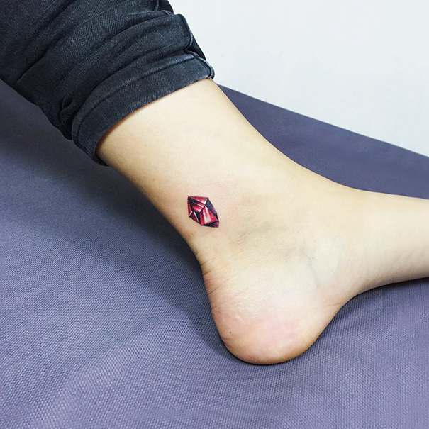 Small foot tattoo with a red gemstone design on the ankle, showcasing minimalist body art.