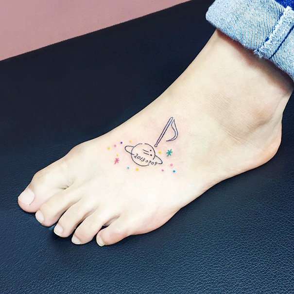 Small foot tattoo of a planet and flag with colorful stars, showcasing minimalist design.