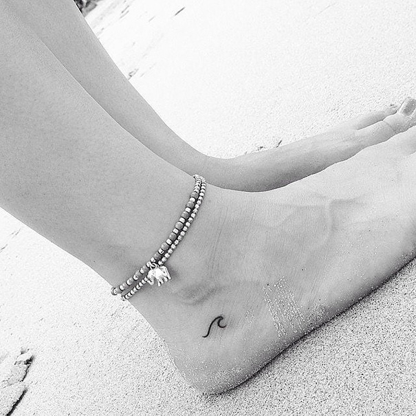 Minimalist small foot tattoo with an anklet on a sandy beach.
