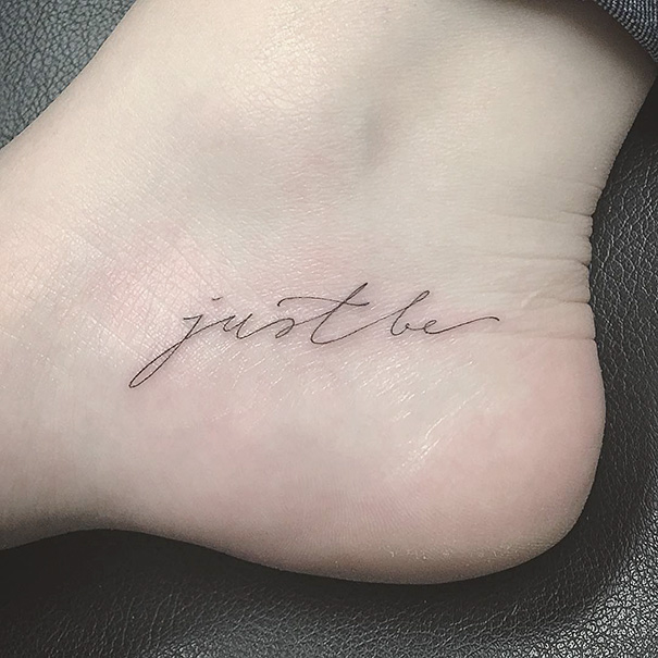 Minimalist small foot tattoo with phrase "just be" in elegant script.