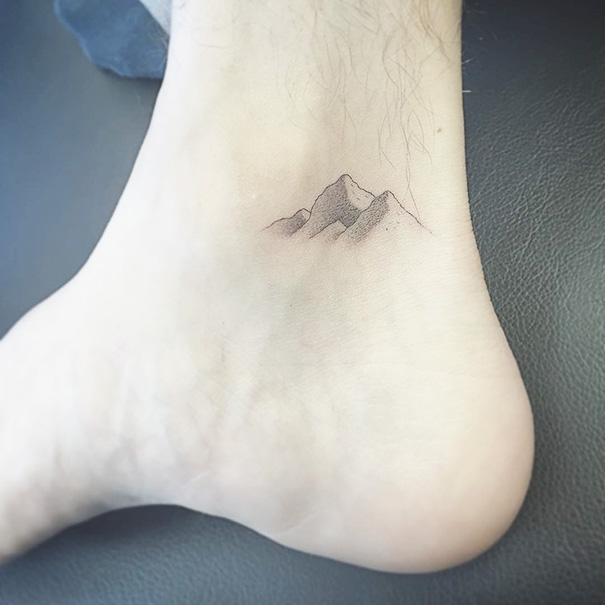 Minimalist small foot tattoo with mountain design, illustrating the concept of less is more in tattoo art.