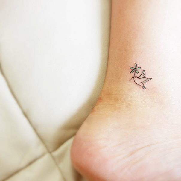 Minimalistic small foot tattoo of a bird with a flower.