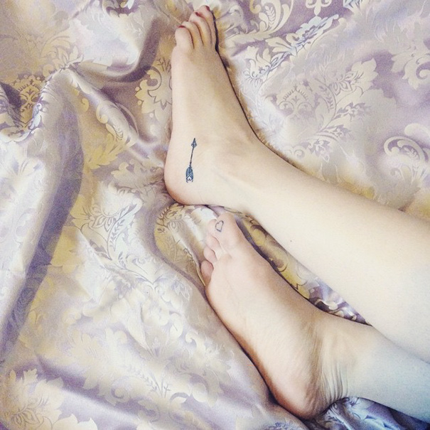 Small foot tattoo with an arrow design on a patterned fabric background.